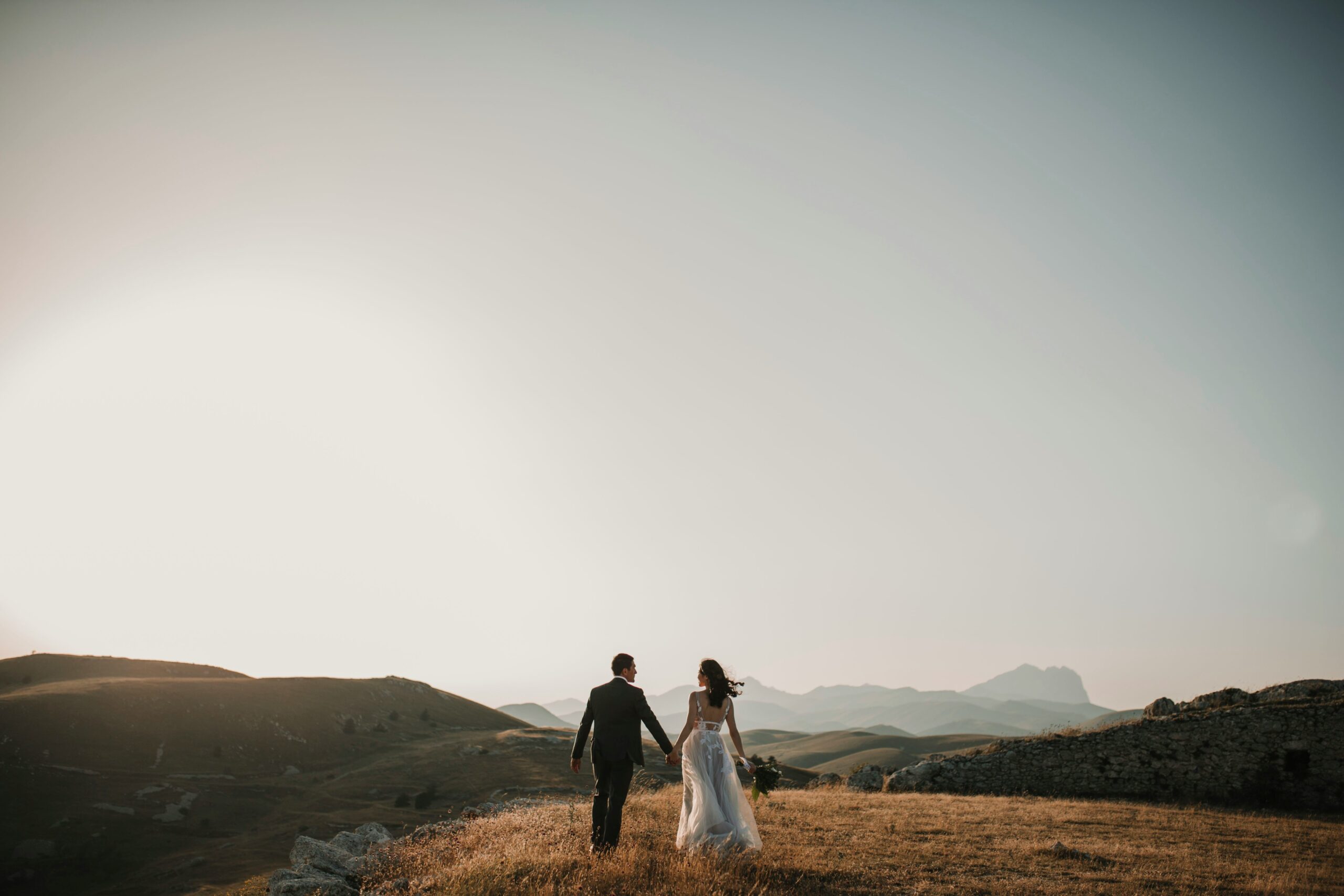 man and woman standing in an open field overlooking mountains